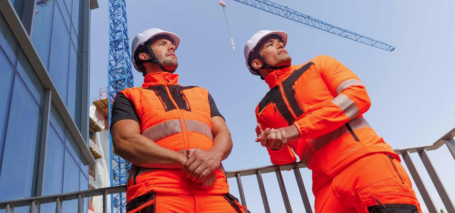Two workers in orange hi-vis jackets on a construction site